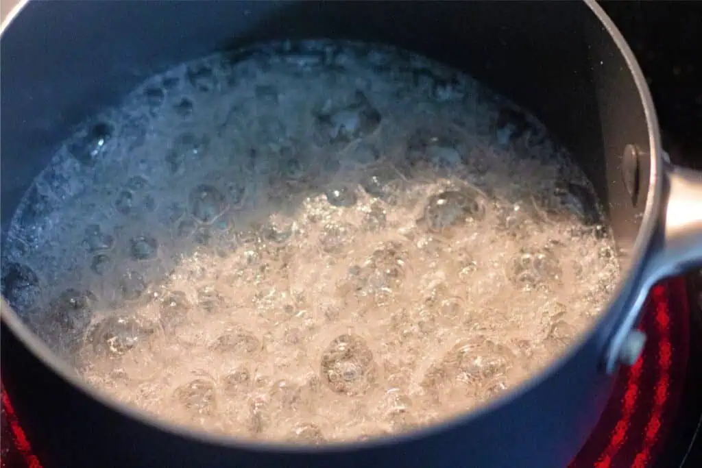 A pot of water, the first step in an easy homemade caramel recipe, boils on the stovetop with bubbles rapidly forming on the surface.