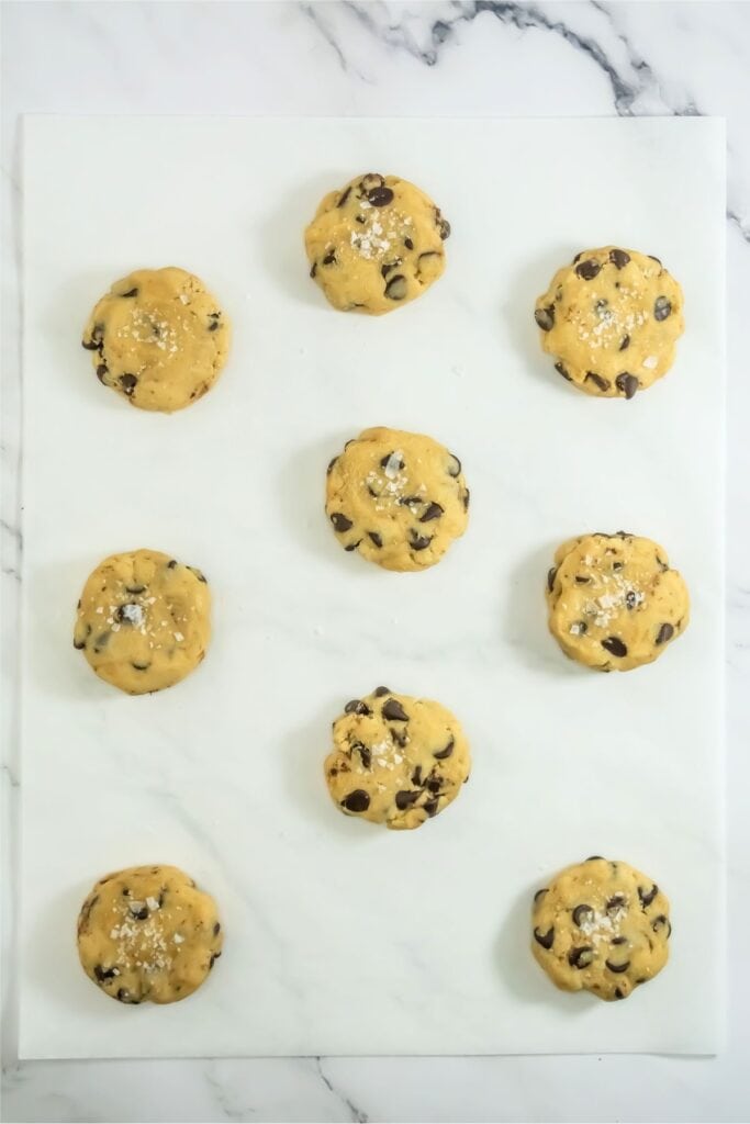 Nine chocolate chip cookies with salt flakes resting on a white marble surface—a perfect example of a sourdough recipe delight.