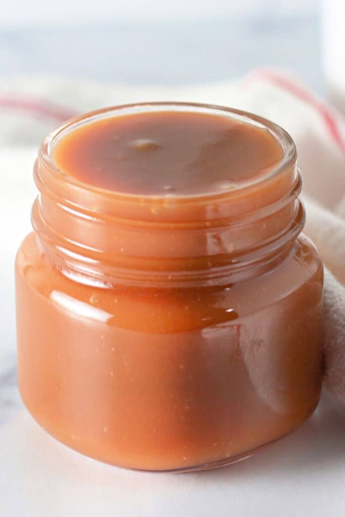 A small jar filled with homemade caramel sauce against a soft background, showcasing the results of an easy caramel recipe.