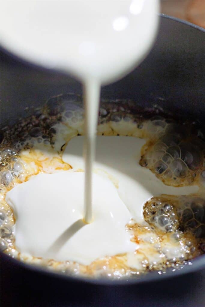 Cream being poured into a pot with a bubbling, homemade caramel-like mixture.