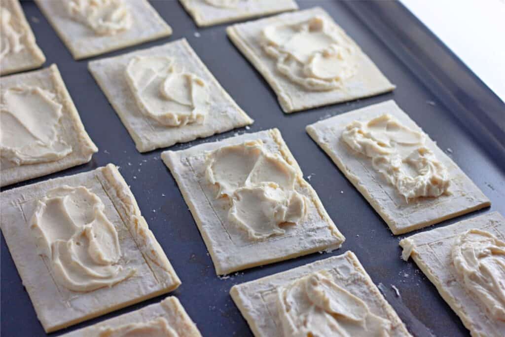 Delicious Cherry Cheesecake Danish squares come to life in this easy recipe: rectangular pieces of pastry dough topped with cream cheese and cherries, ready to bake on a tray.