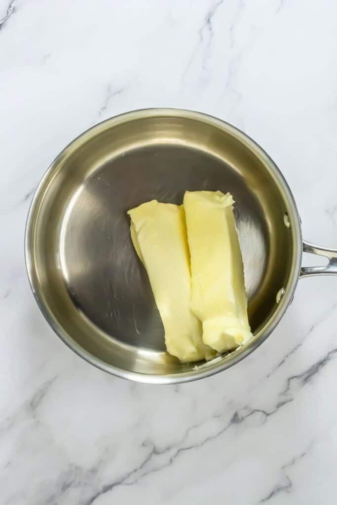 Two sticks of butter in a stainless steel pot on a marble surface, ready to melt into the ultimate chocolate chip cookie recipe.