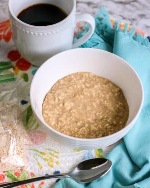 A bowl of instant oatmeal sits invitingly, with a spoon resting beside it and a cup of black coffee on a floral-patterned tablecloth.
