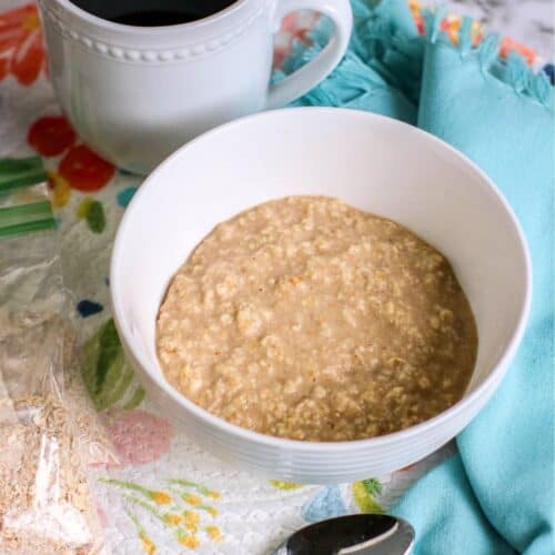 A bowl of instant oatmeal sits invitingly, with a spoon resting beside it and a cup of black coffee on a floral-patterned tablecloth.