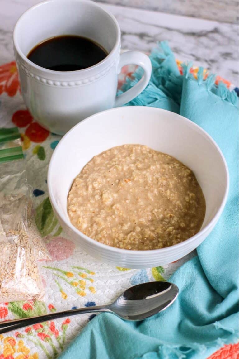 A bowl of instant oatmeal sits invitingly, with a spoon resting beside it and a cup of black coffee on a floral-patterned tablecloth.