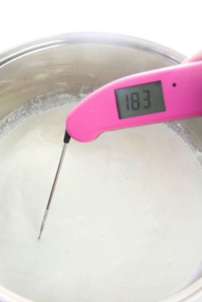 A pink digital thermometer displays 183 degrees Fahrenheit, inserted into a pot of heated milk, the perfect start for a homemade ricotta recipe.