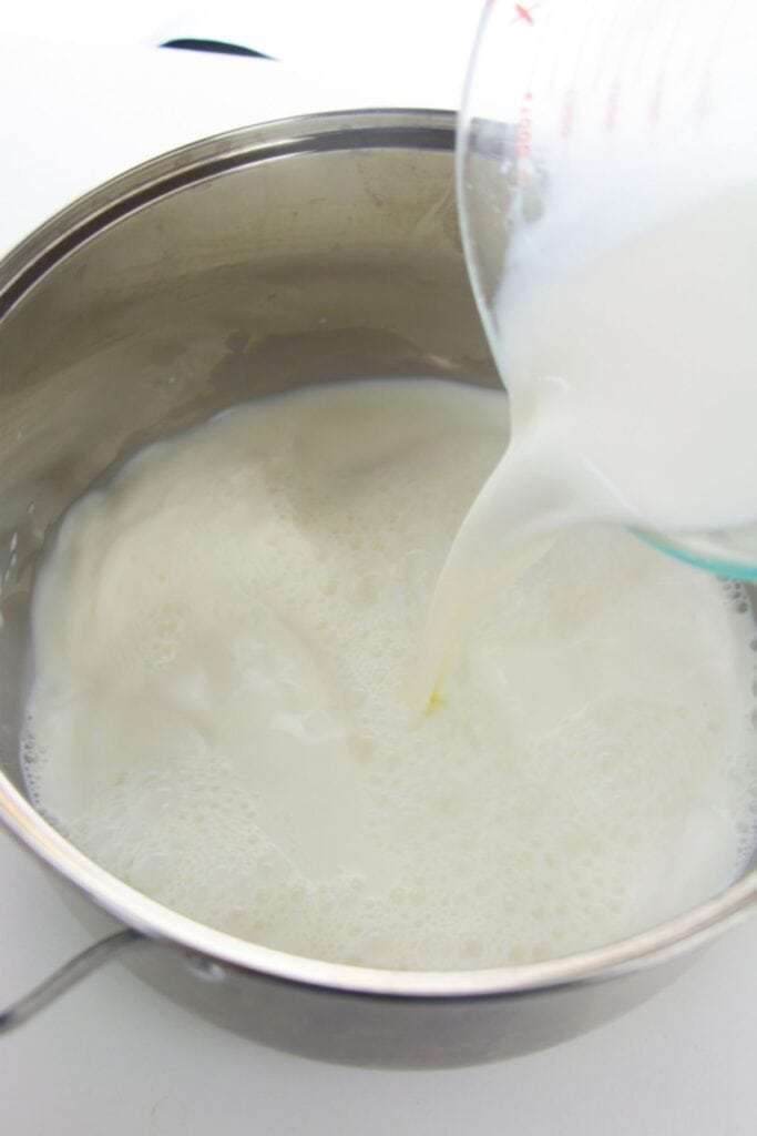 Milk being carefully poured from a measuring cup into a metal pot sets the stage for a delicious homemade ricotta recipe.
