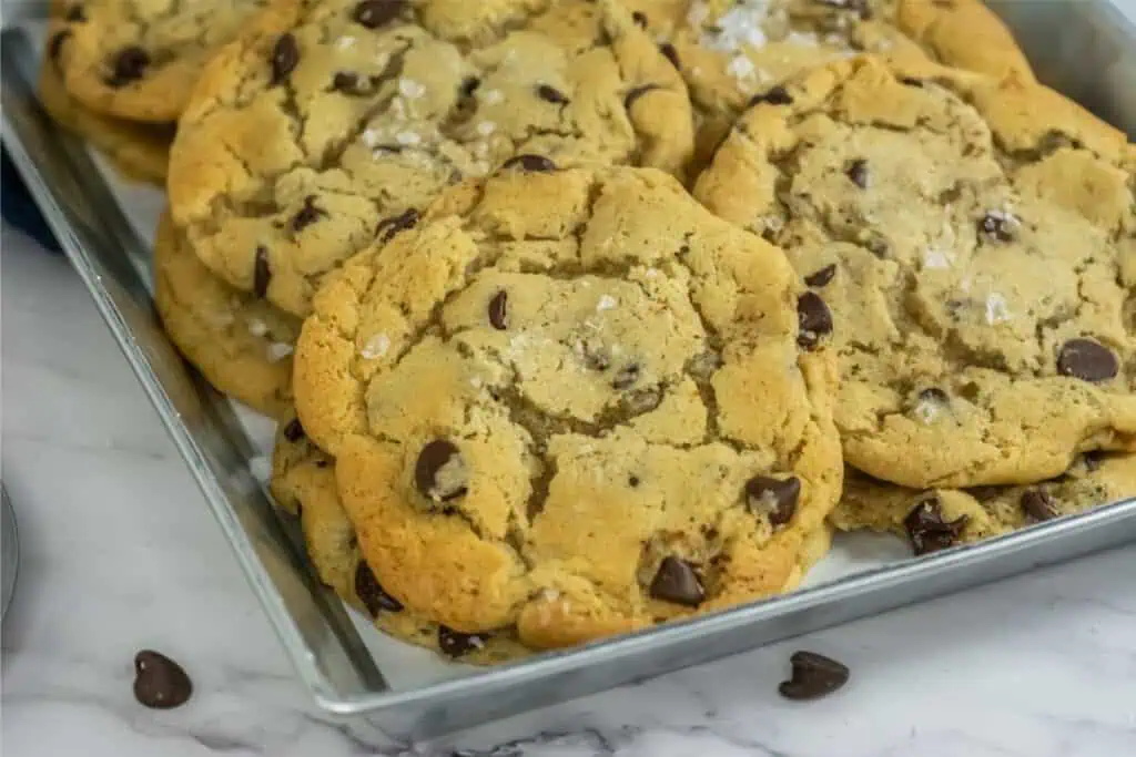 A tray of freshly baked chocolate chip cookies, crafted from a delightfully simple recipe and sprinkled with sea salt, rests invitingly on a marble surface.