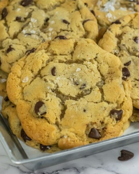 A tray of freshly baked chocolate chip cookies, crafted from a delightfully simple recipe and sprinkled with sea salt, rests invitingly on a marble surface.