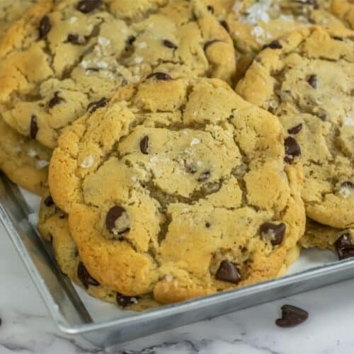 A tray of freshly baked chocolate chip cookies, crafted from a delightfully simple recipe and sprinkled with sea salt, rests invitingly on a marble surface.