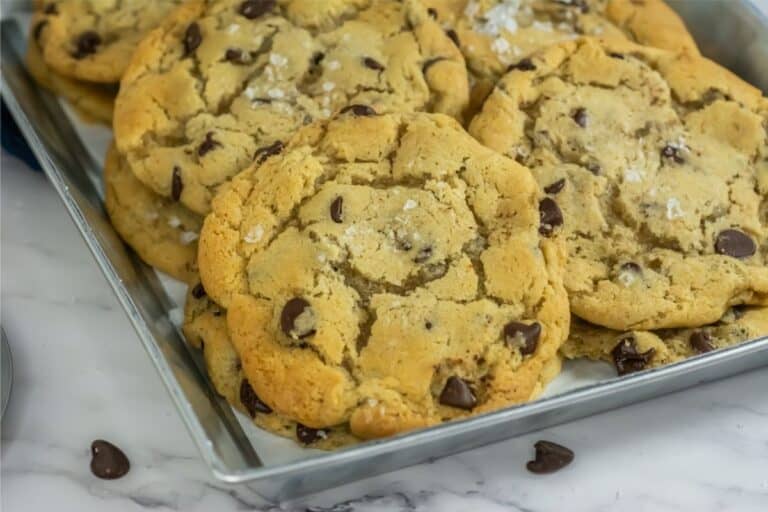 A tray of freshly baked chocolate chip cookies, crafted from a delightfully simple recipe and sprinkled with sea salt, rests invitingly on a marble surface.