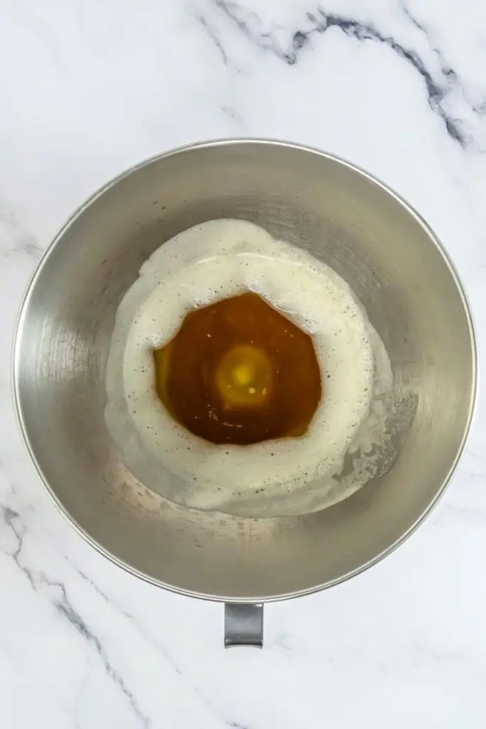 A metal mixing bowl contains flour and a cracked egg in a well, ready for the perfect chocolate chip cookies recipe.