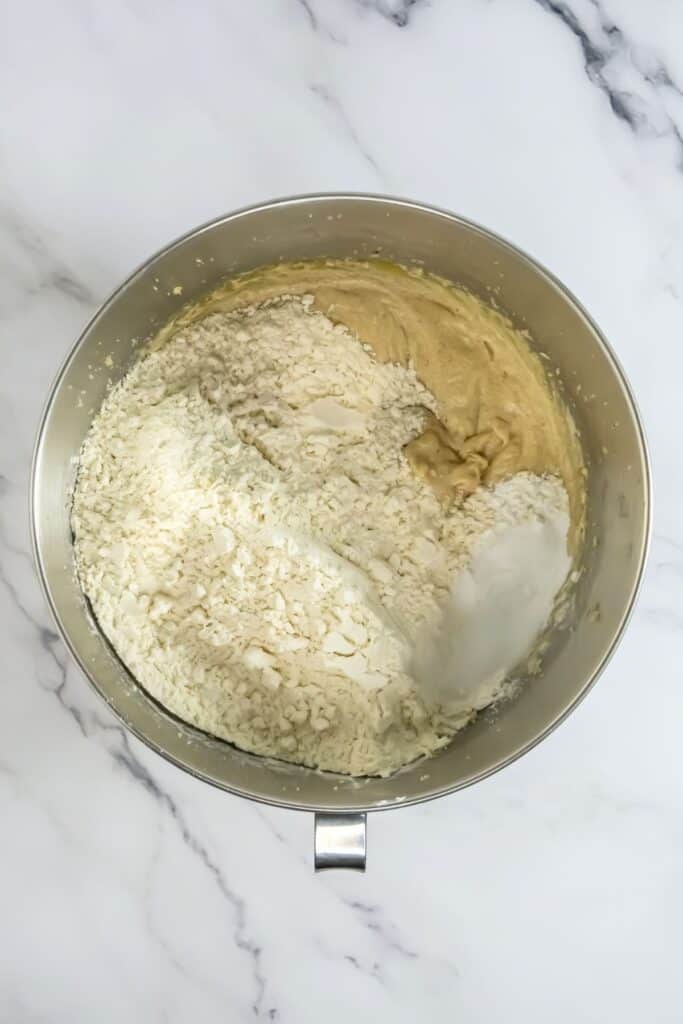 A stainless steel mixing bowl with thick batter and flour being mixed on a marble surface, perfect for whipping up your favorite chocolate chip cookies.