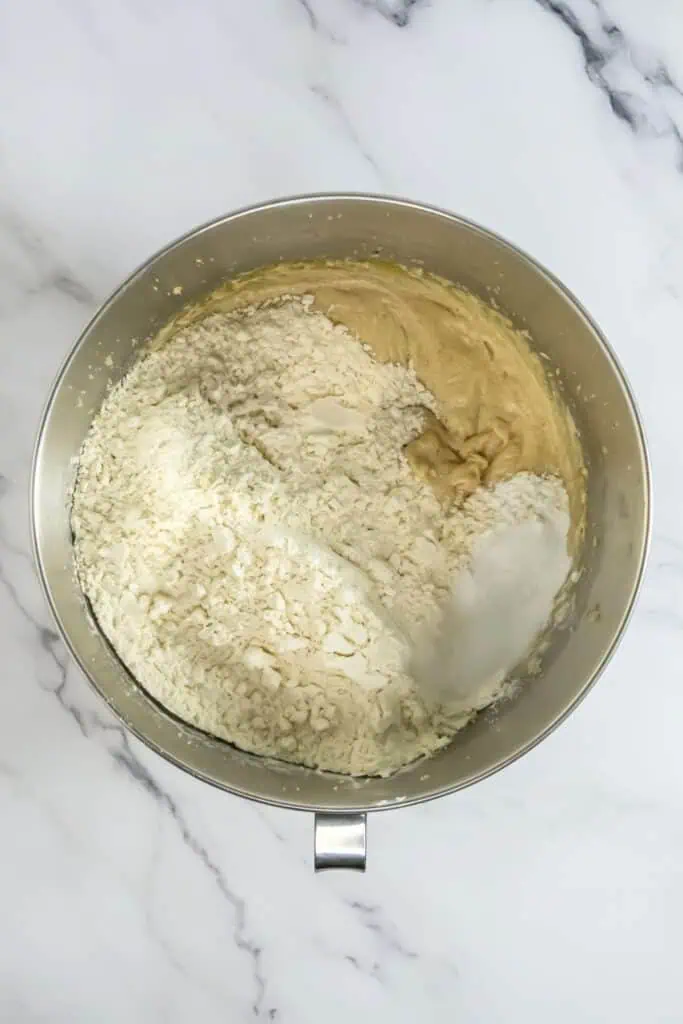 A stainless steel mixing bowl with thick batter and flour being mixed on a marble surface, perfect for whipping up your favorite chocolate chip cookies.