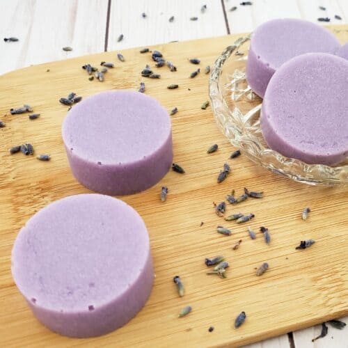 Round lavender soap bars rest on a wooden board, surrounded by scattered dried lavender flowers. These exfoliating bars offer a gentle cleanse, transforming your routine into a soothing ritual.