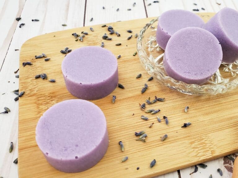 Round lavender soap bars rest on a wooden board, surrounded by scattered dried lavender flowers. These exfoliating bars offer a gentle cleanse, transforming your routine into a soothing ritual.