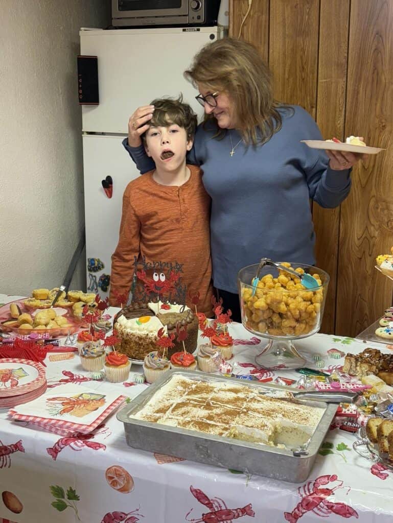 A woman and a boy stand together in front of a table filled with desserts, their bond reflecting the gift of time. The boy is making a playful face, capturing the joy that has only grown in their relationship with mom over the years.
