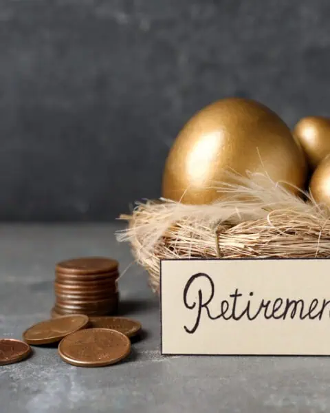 A nest with golden eggs and a "Retirement" sign beside stacked coins on a gray surface, symbolizing thoughtful retirement planning.