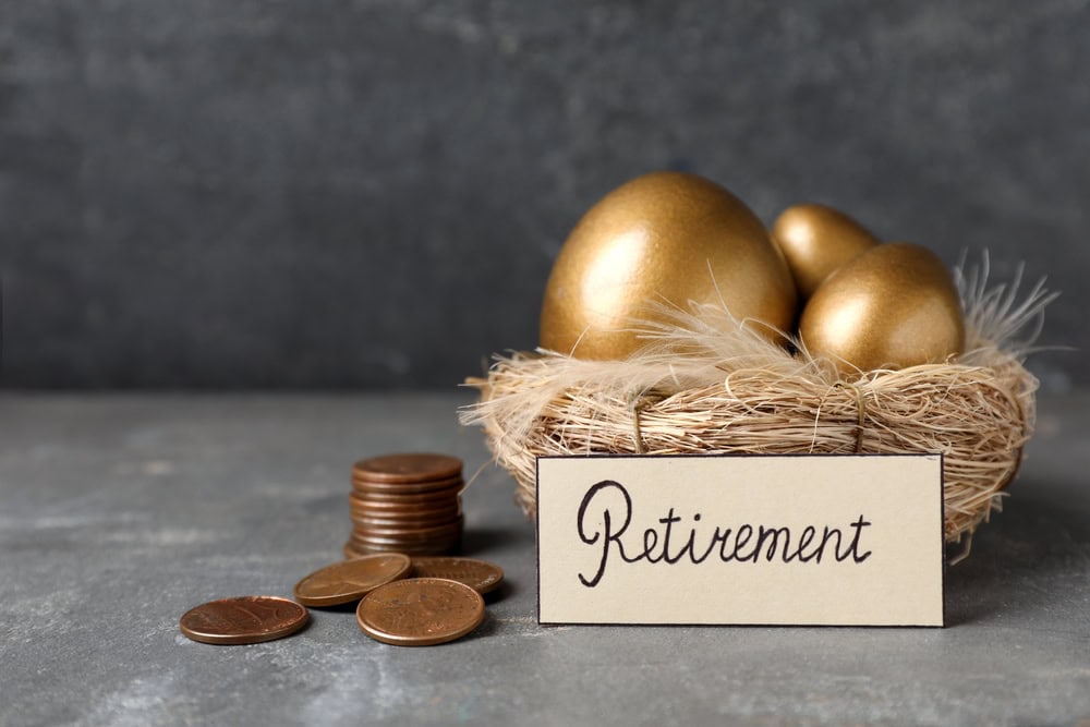 A nest with golden eggs and a "Retirement" sign beside stacked coins on a gray surface, symbolizing thoughtful retirement planning.