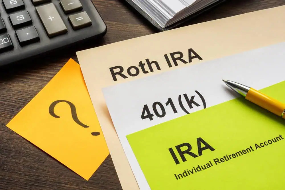 Documents labeled Roth IRA, 401(k), and IRA sit on a table next to a calculator and a paper with a question mark, offering a glimpse into the world of investing and retirement planning.