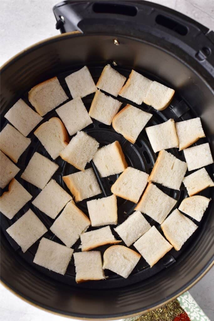Homemade bread cubes neatly arranged in a circular pattern inside an air fryer basket, perfect for turning into crispy breadcrumbs.