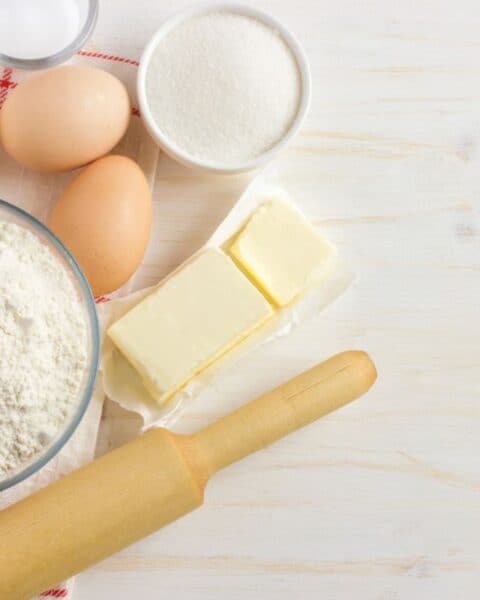 Baking ingredients on a table: flour, eggs, butter, sugar, and milk. A rolling pin is ready for action. Consider substitutions like almond milk or margarine for a twist in your creations.