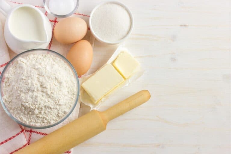Baking ingredients on a table: flour, eggs, butter, sugar, and milk. A rolling pin is ready for action. Consider substitutions like almond milk or margarine for a twist in your creations.