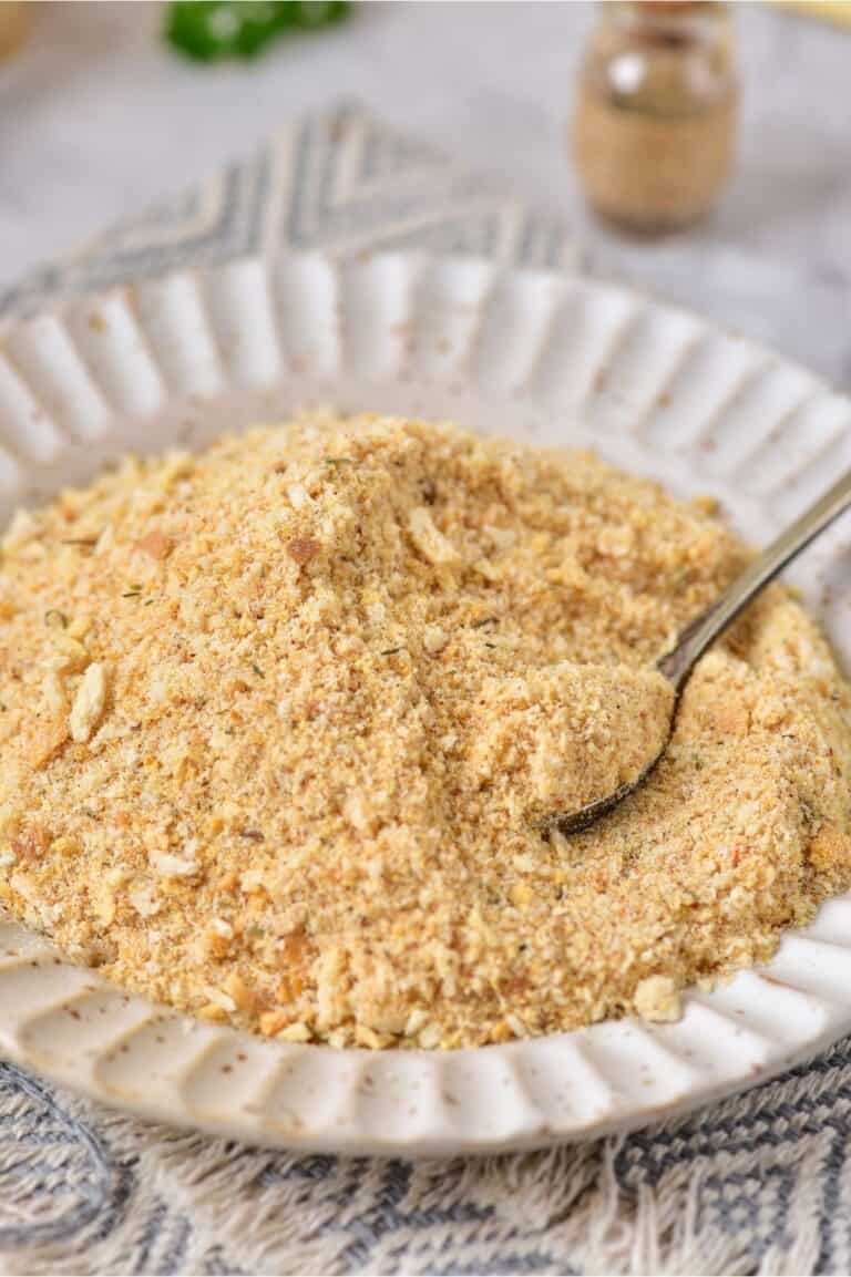 A white plate filled with homemade breadcrumbs, with a spoon partially submerged, rests on a textured cloth.