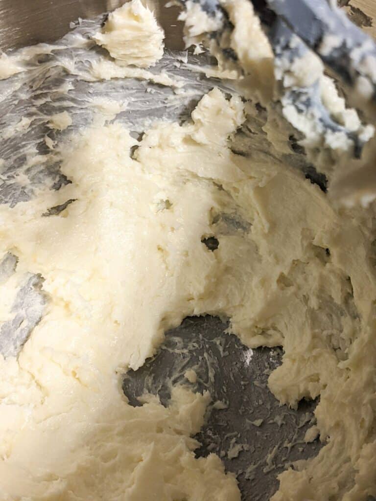 A creamy batter mixture in a metal mixing bowl with a spatula, perfect for crafting delicious condensed milk cookies.