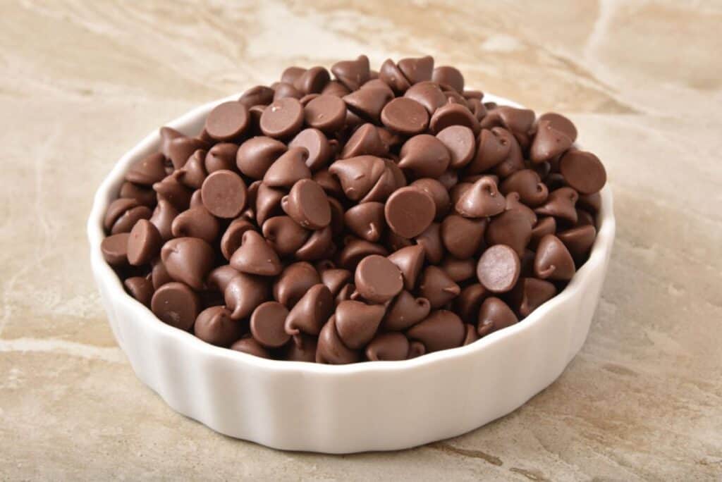 A white bowl brimming with chocolate chips rests on a marbled surface, ready for baking delights or creative substitutions.