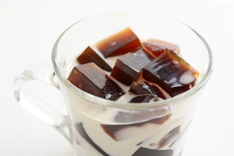 A glass cup brimming with Coffee Jelly cubes and cream rests elegantly on a white background, showcasing a delightful coffee dessert.