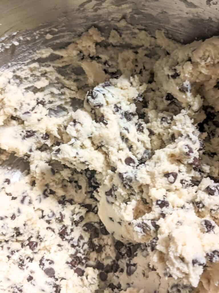 Close-up of creamy chocolate chip cookie dough swirled with sweet condensed milk, showcasing chunks of chocolate chips evenly distributed throughout the light-colored dough.