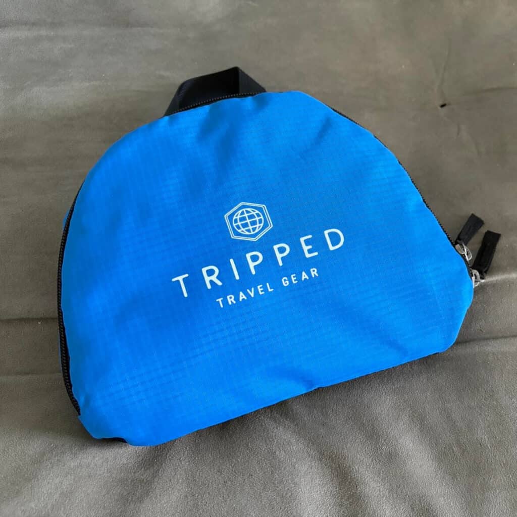 Blue travel gear bag with "TRIPPED TRAVEL GEAR" logo, placed on a gray surface.