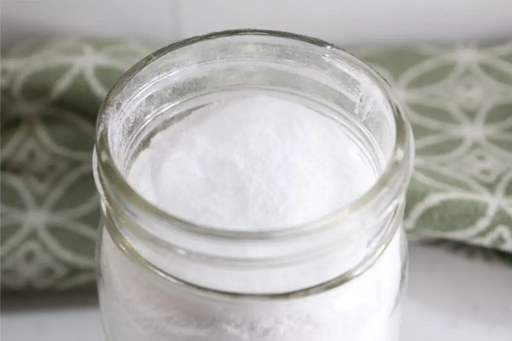 A jar filled with white powder, labeled "Homemade Toilet Cleaner," sits on a surface, with a green patterned cloth in the background.