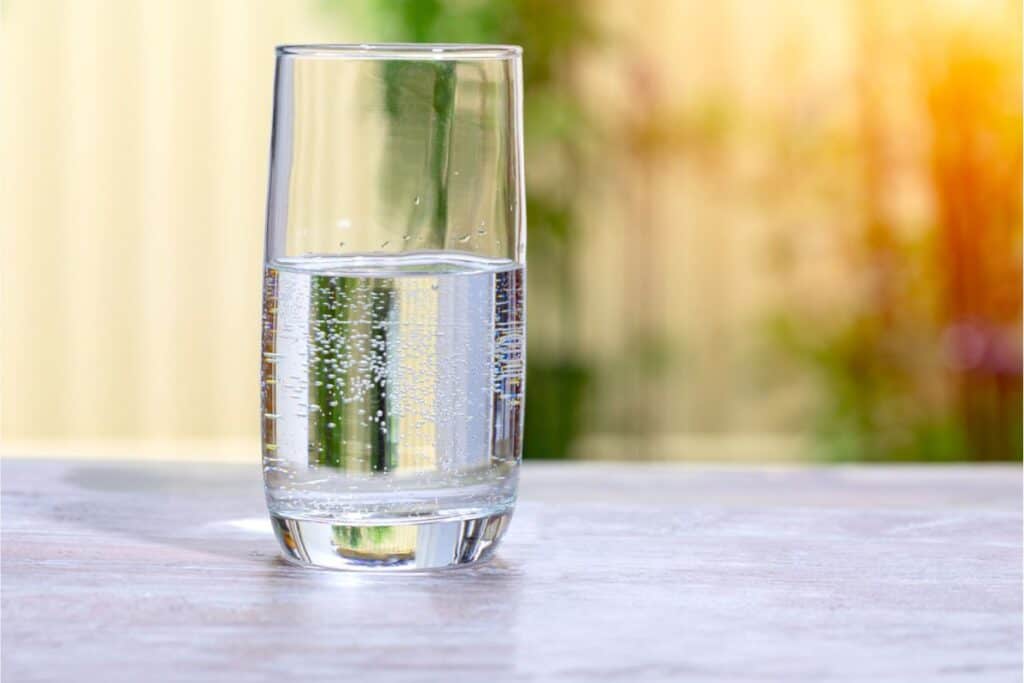A glass of sparkling water sits on a table, promising refreshment and safety, with a blurred outdoor background.