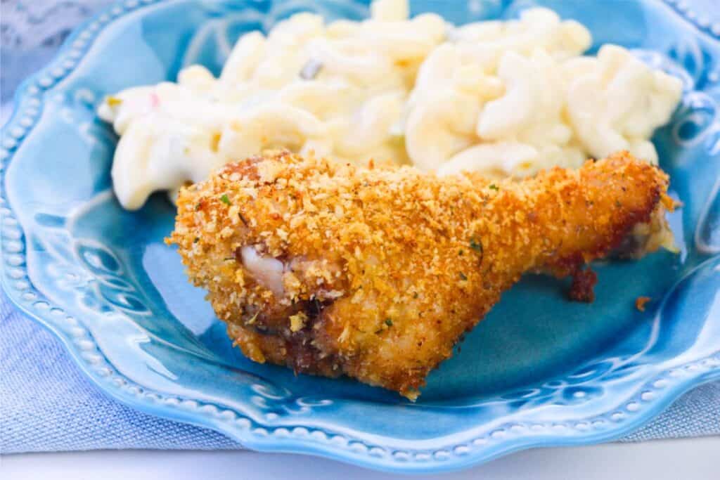 A breaded chicken drumstick made with homemade breadcrumbs and macaroni with cheese served on a blue plate.