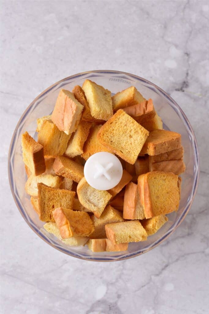 Homemade breadcrumbs in a food processor bowl on a marble surface, ready for blending.