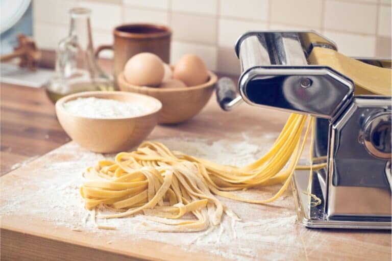 A pasta maker sits elegantly on a wooden surface, surrounded by a bowl of flour and eggs, ready for you to craft your homemade pasta. It’s the perfect setting to dive into your favorite pasta recipe and make fresh noodles from scratch.
