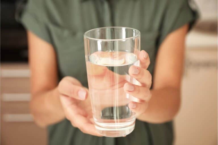 A person wearing a green shirt holds a clear glass filled with water, making sure it's safe to drink.