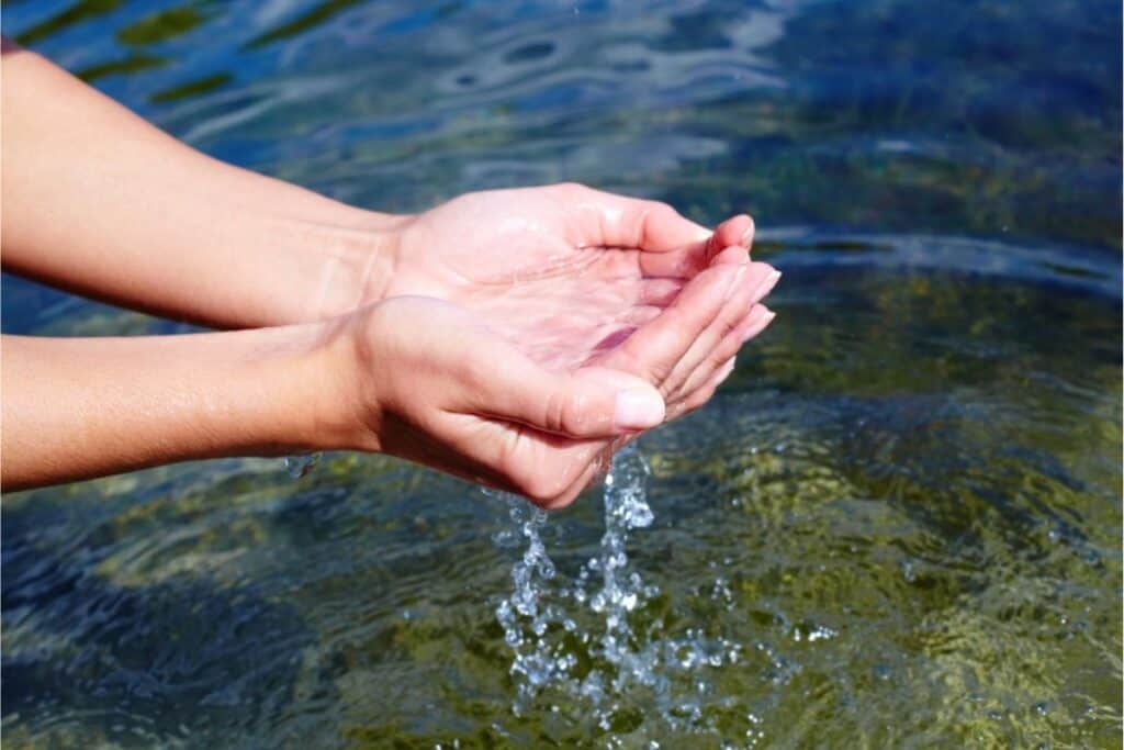 Hands cupping clear water with droplets cascading against a rippling water surface, ensuring it's safe to drink.