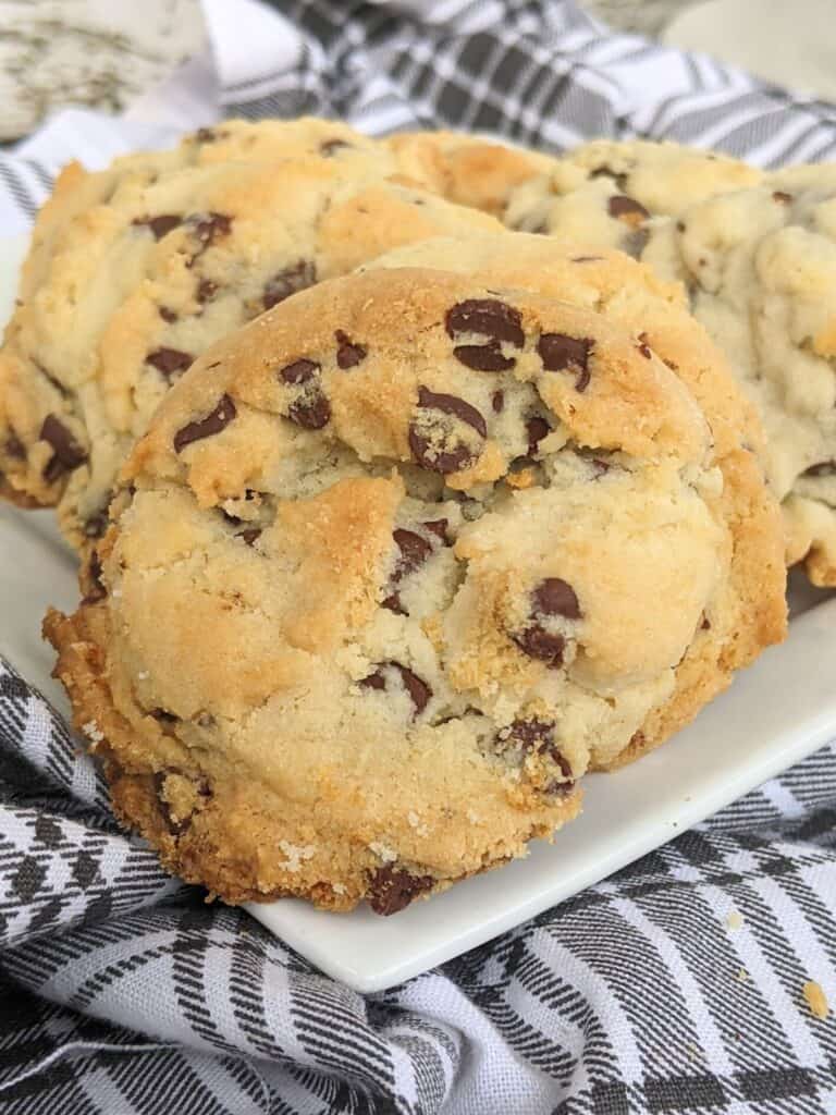 Three chocolate chip cookies on a white plate, nestled atop a black and white checkered cloth, are made extra creamy with the addition of condensed milk.