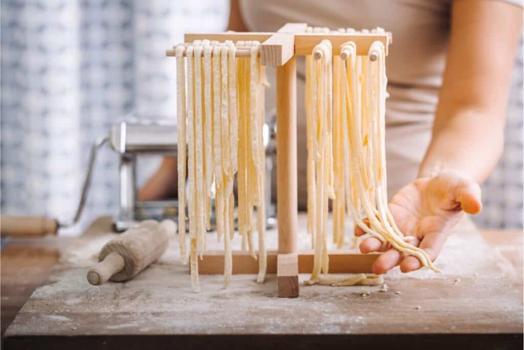 A skilled cook is crafting homemade pasta, expertly using a machine and drying rack on a floured table.