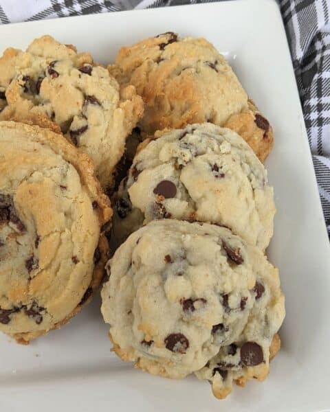 A plate of crinkly chocolate chip cookies, infused with the rich sweetness of condensed milk, rests invitingly on a white plate atop a black and white plaid fabric.