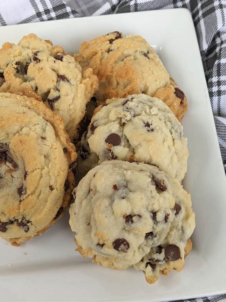 A plate of crinkly chocolate chip cookies, infused with the rich sweetness of condensed milk, rests invitingly on a white plate atop a black and white plaid fabric.