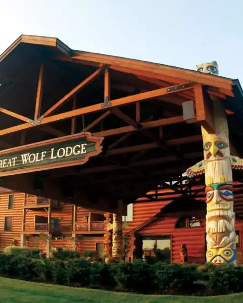The entrance of Great Wolf Lodge features a large wooden canopy, log cabin exterior, and decorative totem poles welcoming guests who scored deals like a Great Wolf Lodge Groupon.