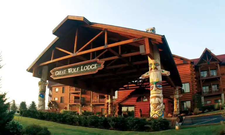 The entrance of Great Wolf Lodge features a large wooden canopy, log cabin exterior, and decorative totem poles welcoming guests who scored deals like a Great Wolf Lodge Groupon.