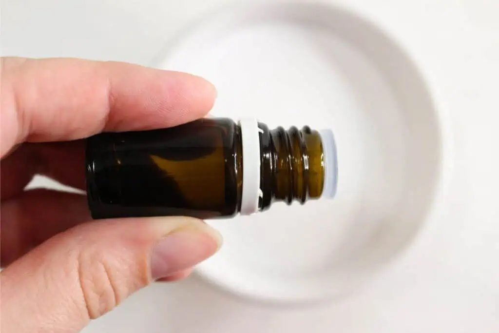 A person holding a small, amber-colored glass bottle with a white cap stands against a white background, appearing to showcase an elegant homemade cleaner.