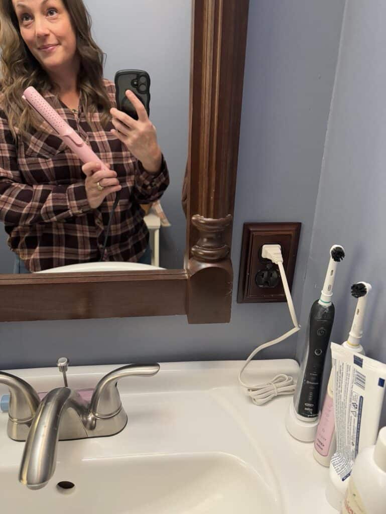 In a personal post, a person in a plaid shirt snaps a selfie in the bathroom mirror, clutching a pink hairbrush. An electric toothbrush and sink faucet frame the scene subtly.
