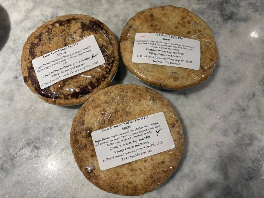 On a marble surface, three individually wrapped Little Giant Pies steal the spotlight in this personal post, featuring delightful Shoo-Fly, Apple, and Fruit of the Forest varieties.