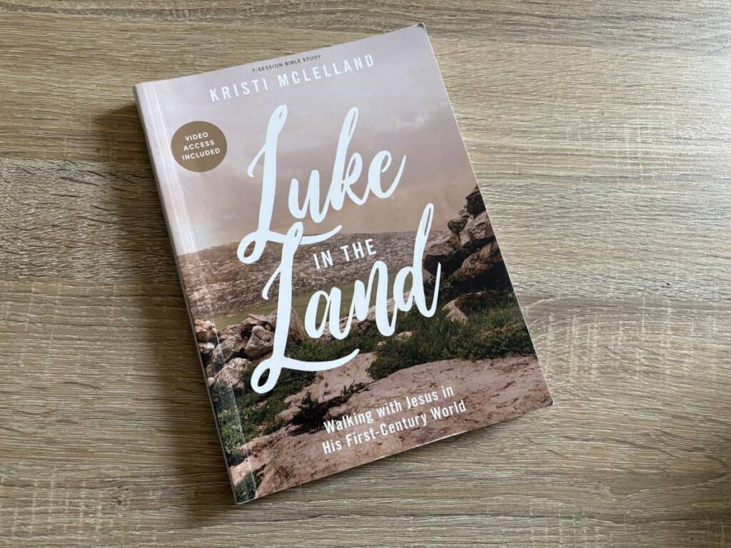 The cover of "Luke in the Land" by Kristi McLelland captures a personal journey, showcasing a desert landscape with rocky terrain, subtly positioned on a wooden surface.